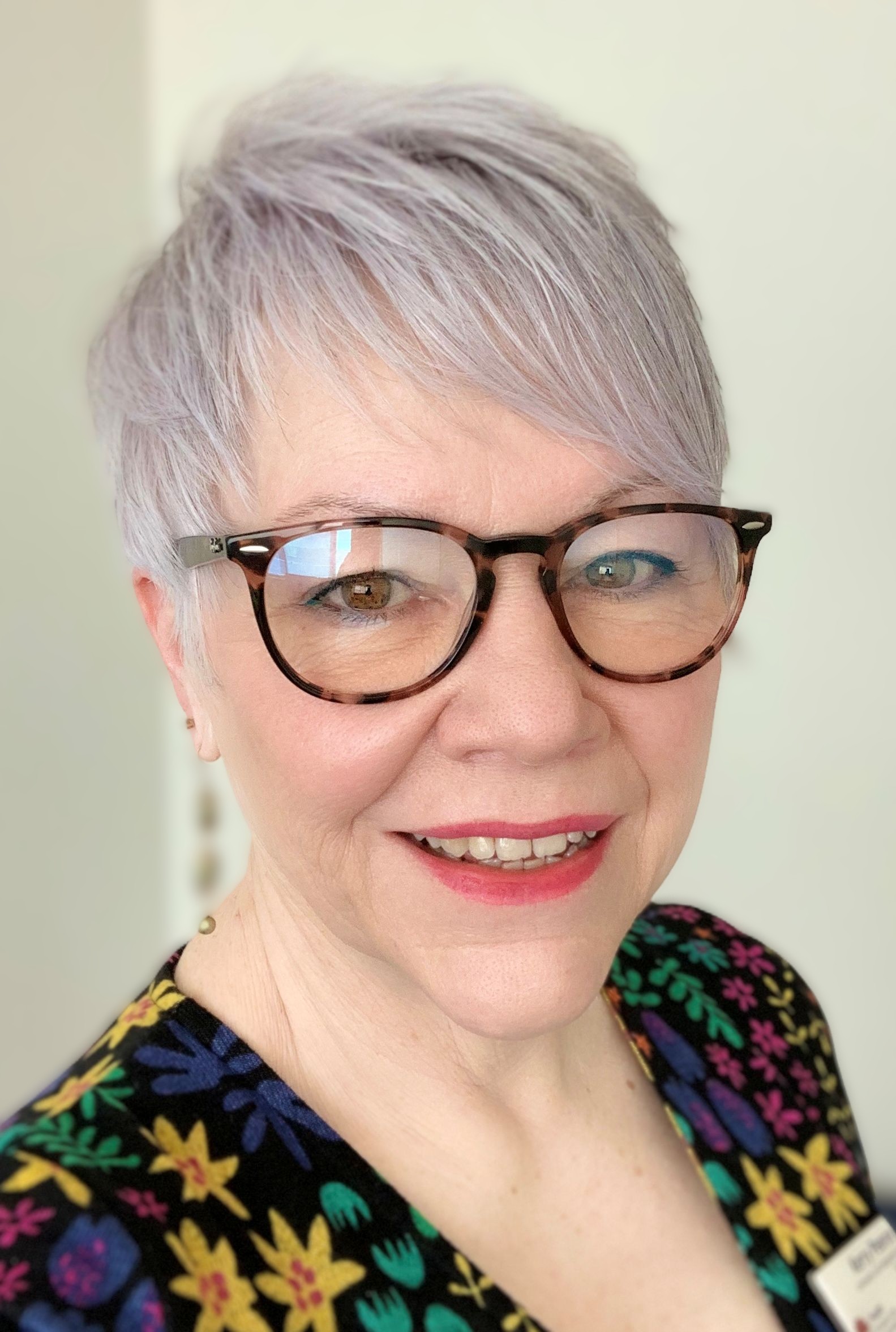 Portrait photo of Principal Occupational Therapist, Kerry Pearce, smiling warmly at the camera. Kerry is Caucasian, aged in her early 60's, is wearing glasses and has short, grey hair. She is wearing a floral dress.